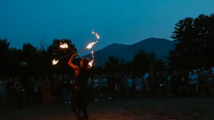 Fire dancer seen twirling flaming batons at music festival at dusk