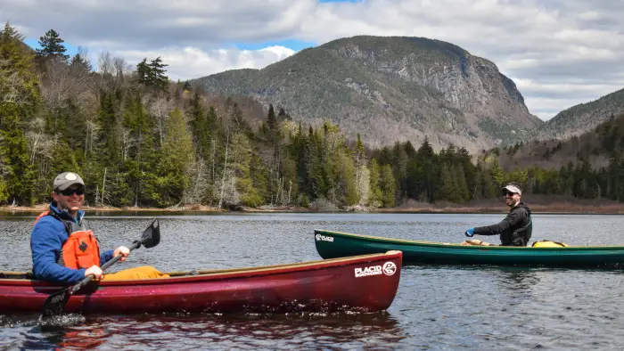 Two paddlers on the water in front of a tall mountain with steep cliffs