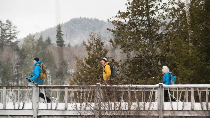 Three people snowshoeing across a bridge at the AIC