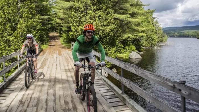 two men bike across a wood bridge.