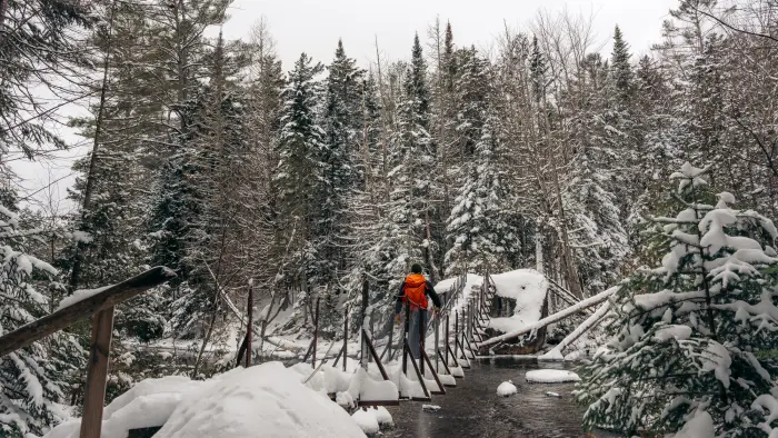 A hiker going over a metal bridge in the winter