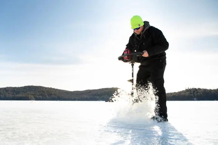 A man with an ice auger drilling a hole for ice fishing.