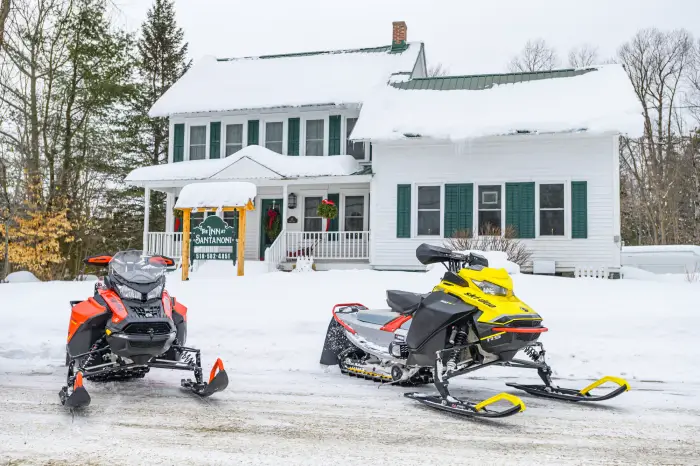 Two snowmobiles (one red&#44; one yellow) are parked in front of a charming&#44; white and green country inn.