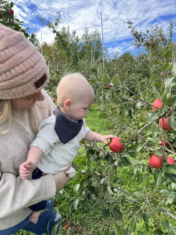 A mom and her baby pick an apple off the tree.