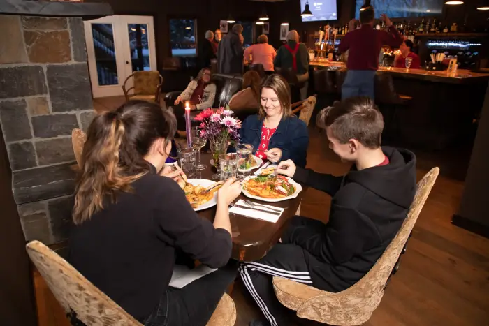 A woman and two teenagers sit at a table&#44; eating&#44; at a lively restaurant.
