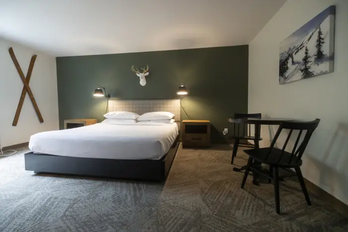A hotel room featuring modern Adirondack decor&#44; a large bed&#44; and charming antique chairs.