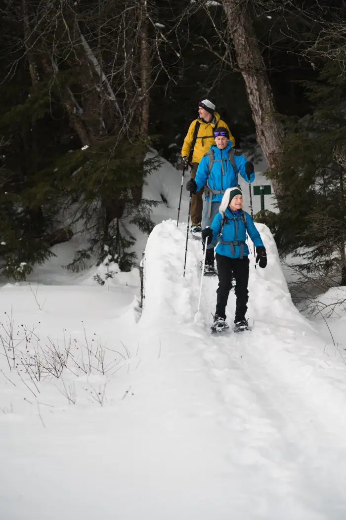 Three hikers walk down a slope on a snow covered trail.