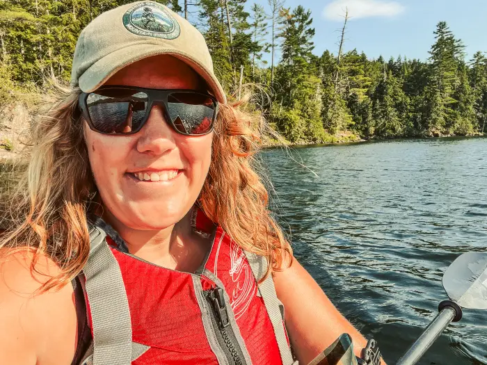 A beautiful blonde haired woman smiling in her canoe wearing sunglasses