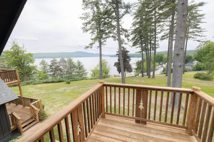 A wooden deck looks out over a tree-ringed grassy lawn&#44; with a lake beyond.