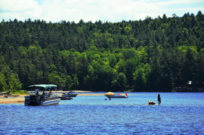 A woman sits on the end of a boat near a child in a life jacket who is about to go swimming.