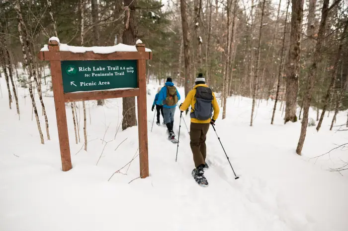 three snowshoe hikers pass a sign for Rich Lake Trail.