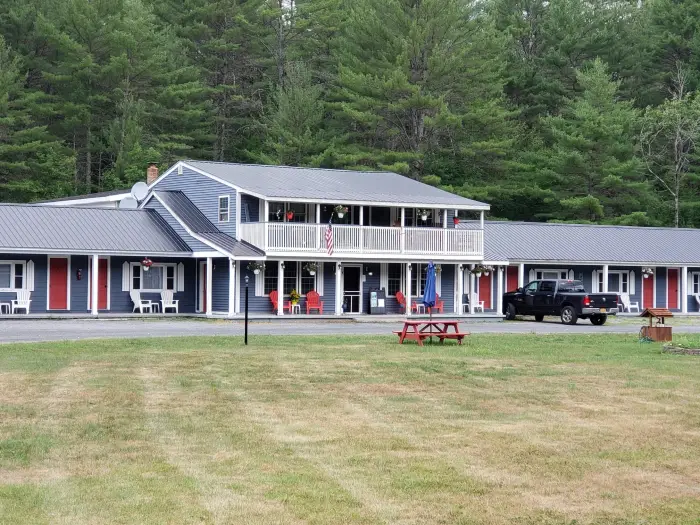 The exterior of a tidy&#44; two-story blue and white motel with evergreen trees in the background.