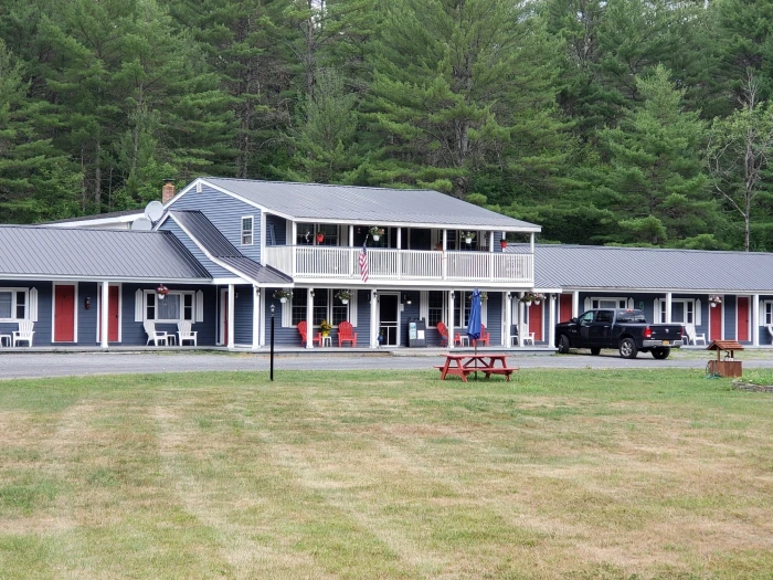 The exterior of a tidy&#44; two-story blue and white motel with evergreen trees in the background.