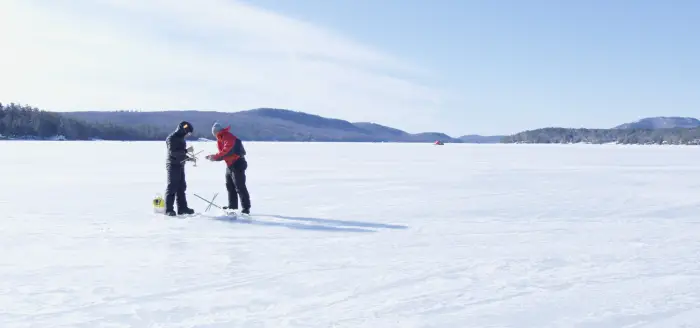 A couple ice fishers on a frozen lake amongst the mountains