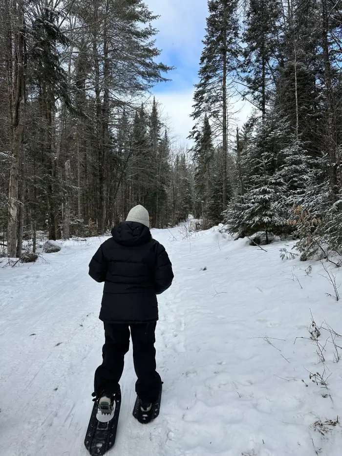 A woman snowshoes down a snowy trail.