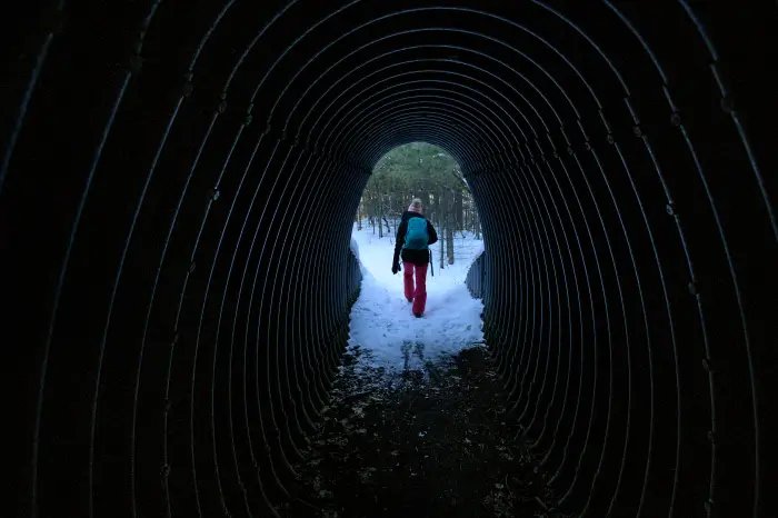 Woman walking through tunnel under a highway.