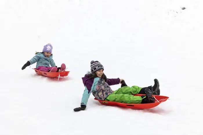 Two kids sledding down a snowy hill.