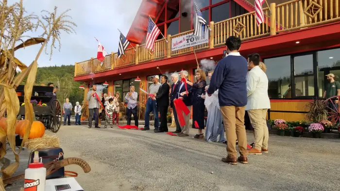 A line of people cut a red ribbon in front of a new&#44; Adirondack-style building.