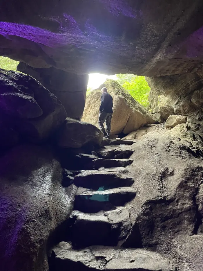 a man climbs out of a purple toned cave into the sun.