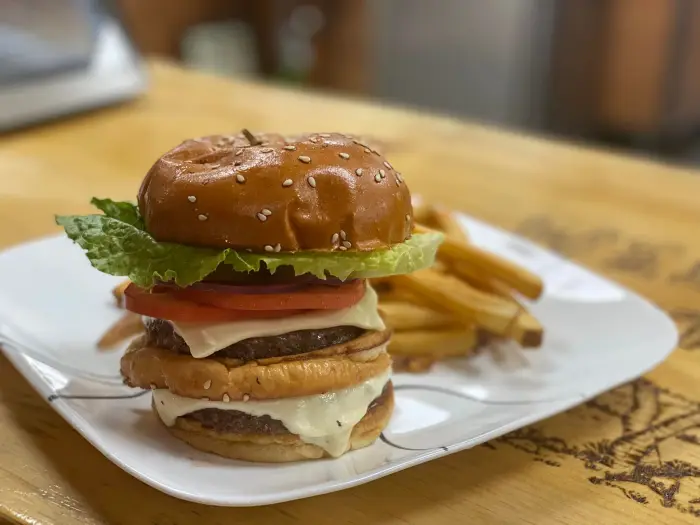 Close up of a tall&#44; stacked cheeseburger on a rustic wooden table.