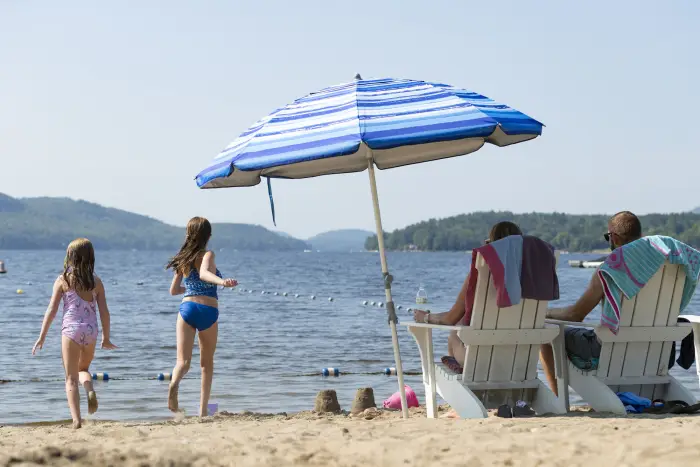 Two children run into the water while two parents relax on the beach in Adirondack chairs