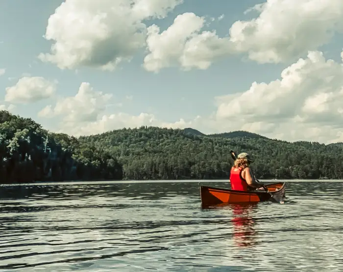 A woman paddling a solo canoe on a lake.