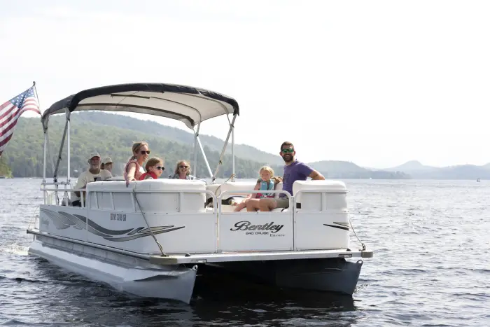 A large family rides in a pontoon boat on the lake.