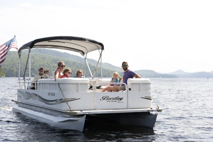 A family group relaxes on a pontoon boat on an Adirondack lake.