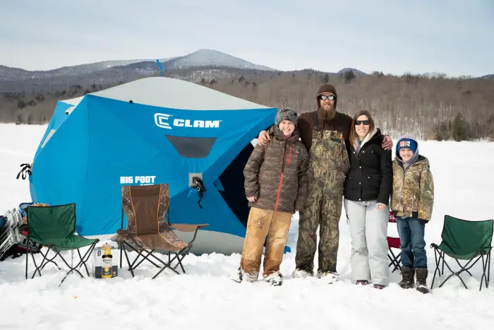 A family posing for a photo in front of an ice fishing tent.