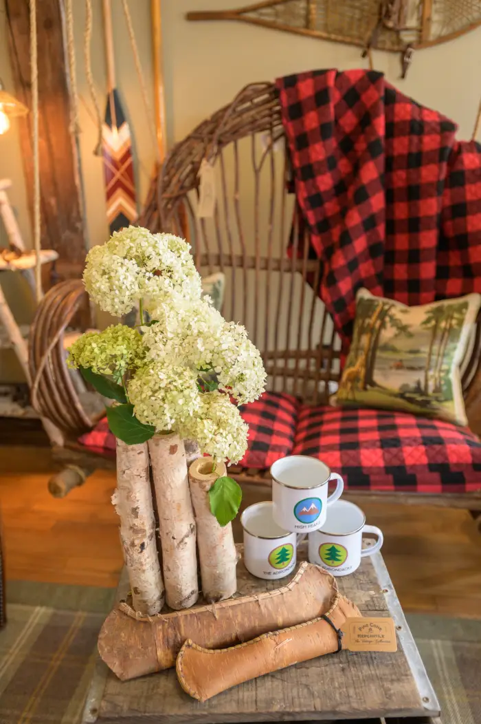 Flowers in a birch tree vase and tin camping mugs on display in an Adirondack-themed gift shop.