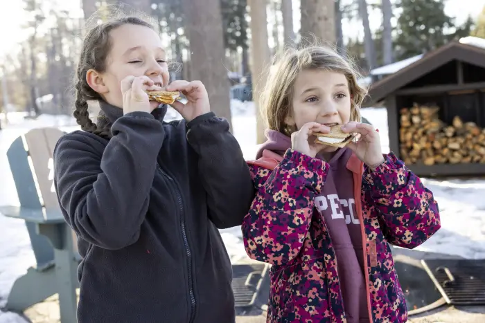 Two young girls eating s'mores outside in the winter.