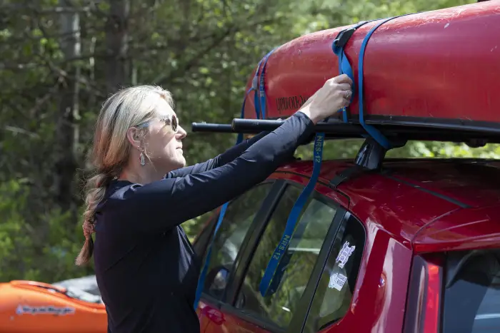 a woman straps in her canoe to the top of a car.