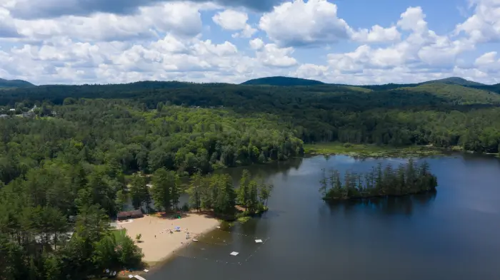 An aerial view of an Adirondack lake and sandy beach&#44; surrounded by thick forests.
