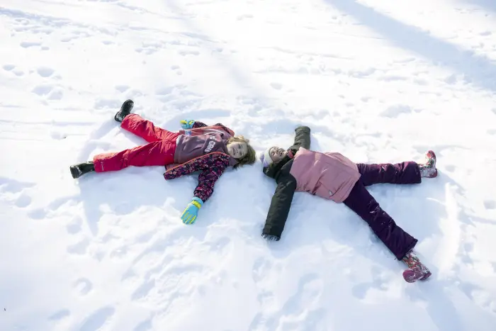 Two young girls making snow angles on a snowy field.