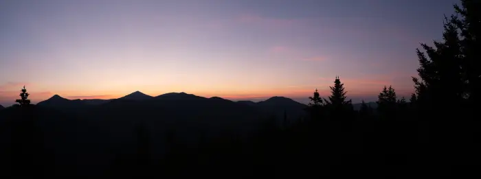 A colorful sunrise silhouettes mountains and trees.