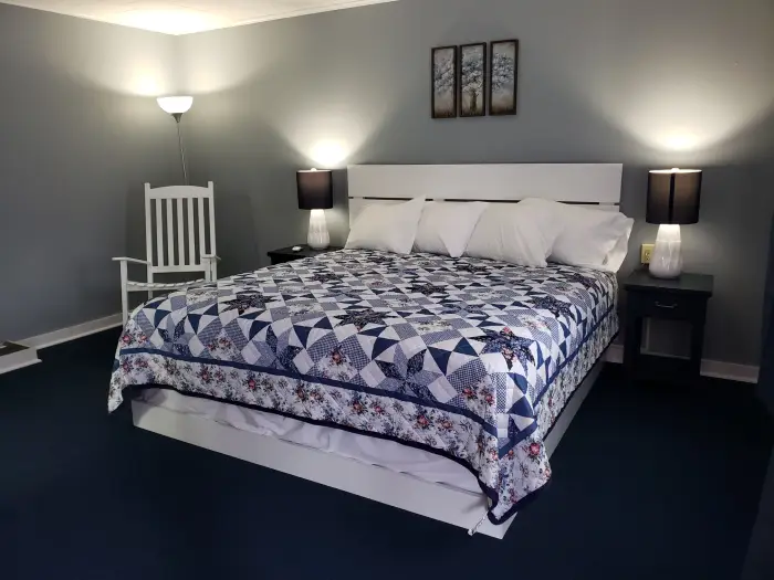 A cheerful&#44; clean motel room featuring a colorful quilt and Adirondack rocking chair.