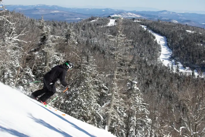 A skier going down a slope with a mountain lodge in the background