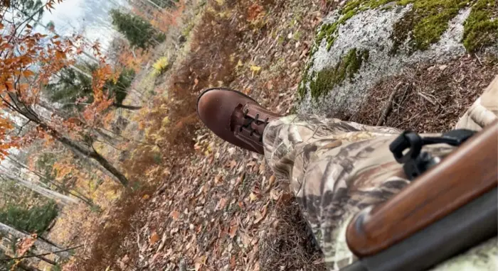 Hunter laying by a tree waiting for a deer with a gun in hand