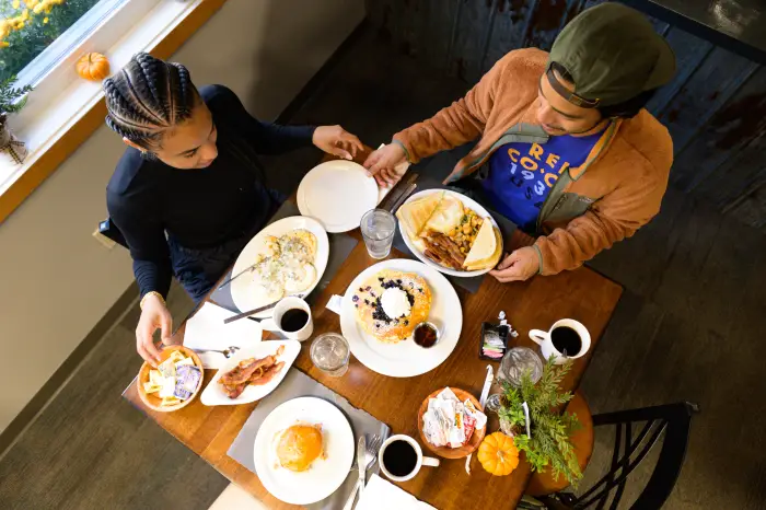 An overhead shot of a man and woman sharing mutliple plates of breakfast food at a cafe.