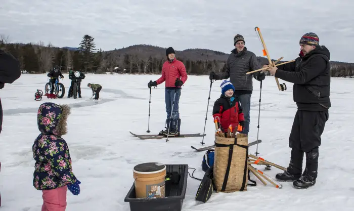 A group of people and children on a lake participating in ice fishing&#44; cross-country skiing&#44; and fat tire biking.