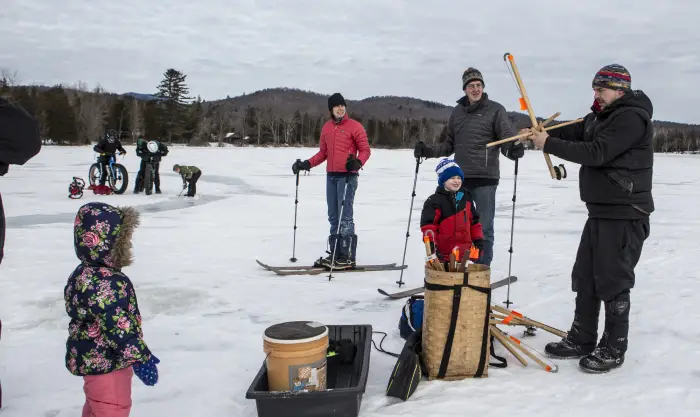 Adults and kids drill through the ice to ice fish.
