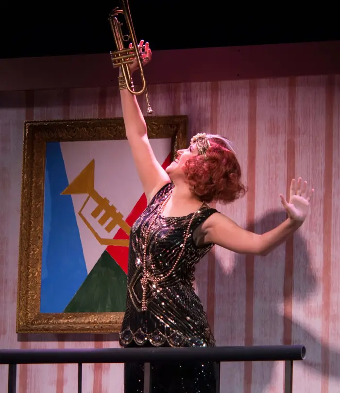 A female performer in 1920s themed costume sings with a trumpet before a jazz backdrop.