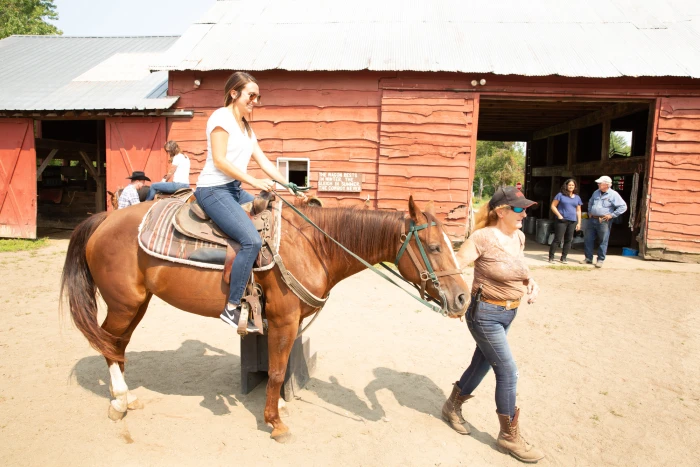 two girls ride on horseback on a wooded trail.