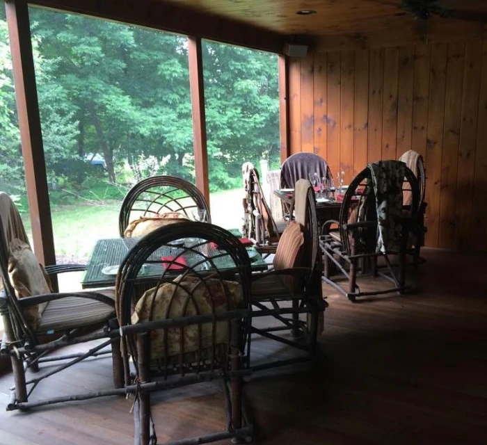 Large bent twig chairs surround square dinner tables at a restaurant with a view of woods.