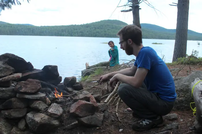 A man and a woman cook their dinner over a campfire in the backcountry.