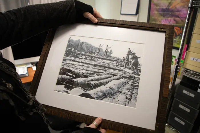 A person's hands hold a printed photo of a historic logging operation