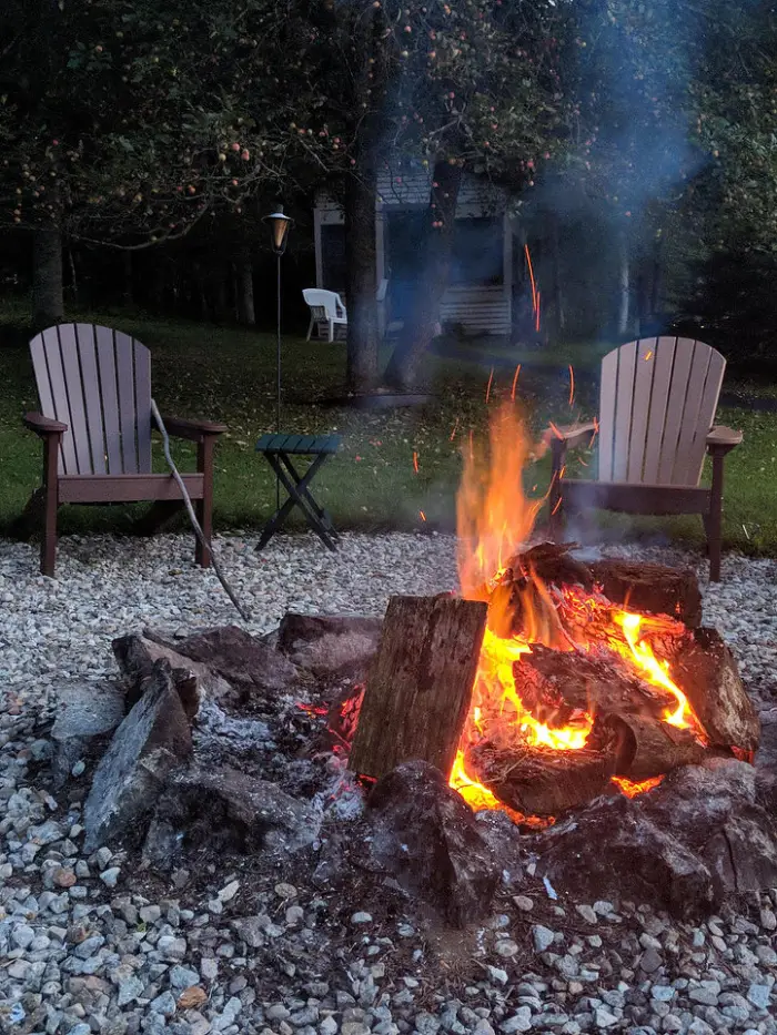 Fire going in a fire pit with Adirondack chairs around it.