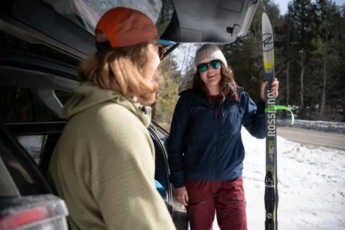 Two people talk at the back of a car with xc ski gear