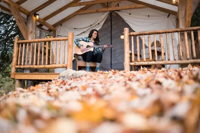 A woman plays guitar on the front porch of a wooden glamping tent