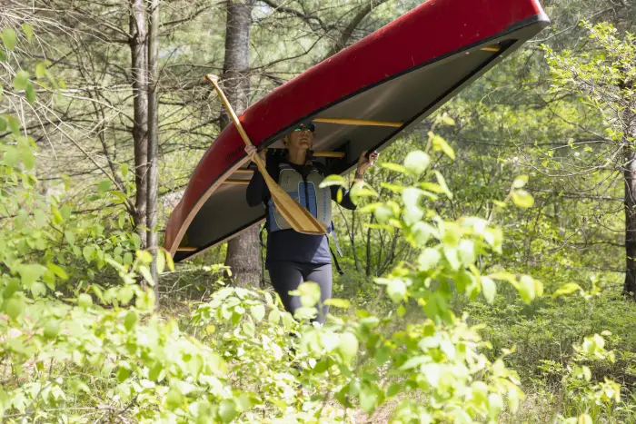 Two teenage girls paddle kayaks on a sunny day with forest in the background.